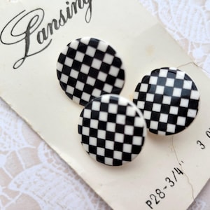 May include: Three black and white checkered buttons on a vintage card. The buttons are round with a glossy finish. The card has the word "Lansing" in cursive and the measurement "P28-3/4" printed on it.
