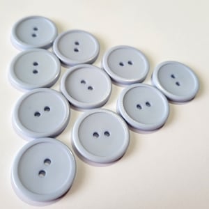 May include: Ten light blue plastic buttons with two holes each. The buttons are arranged in a triangular shape.