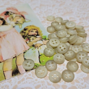 May include: A pile of off-white plastic buttons with four holes each. The buttons are arranged in a random pattern and are all the same size.
