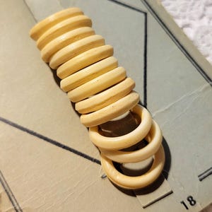 May include: A vertical stack of ten pale yellow circular rings attached to a light tan rectangular card. The card features black geometric lines and the printed text No. 18 in the bottom right corner. The rings have a smooth, rounded finish.