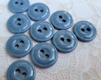 May include: Ten blue plastic buttons with two holes each. The buttons are arranged in a semi-circle on a white lace background.