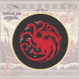 May include: A red three-headed dragon embroidered on black fabric in a circular wooden embroidery hoop. The dragon is a popular symbol from the TV show Game of Thrones.