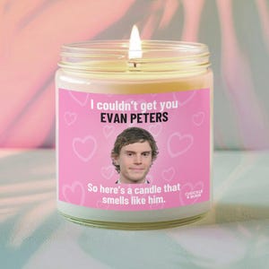 Peut inclure: Une bougie allumée dans un bocal en verre avec une étiquette rose. L'étiquette comporte le texte "I couldn't get you EVAN PETERS" et "So here's a candle that smells like him." avec une photo d'un homme. La bougie est de CHUCKLE & BURN.