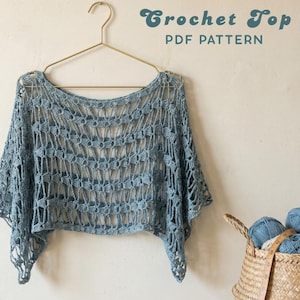 Könnte beinhalten: Hellblaues Häkeltop mit einzigartigem offenem Webmuster, an einem goldenen Kleiderbügel aufgehängt. Der Text "Crochet Top PDF Pattern" steht über dem Top. Ein Korb mit blauer und weißer Wolle befindet sich im Hintergrund.