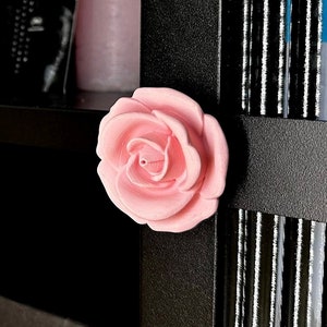 May include: A pink rose-shaped decorative knob attached to a black cabinet door.