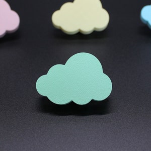 Könnte beinhalten: Vier hölzerne Wolkenformen in verschiedenen Farben: rosa, gelb, hellblau und grün. Die Wolken sind auf einer schwarzen Oberfläche angeordnet.