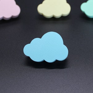 Può includere: Quattro forme di nuvole in legno di diversi colori: rosa, giallo, azzurro e verde. Le nuvole sono disposte a semicerchio su uno sfondo nero.