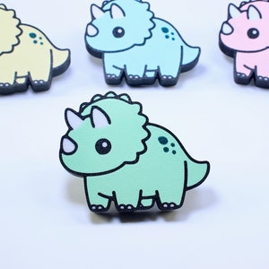 Könnte beinhalten: Vier kleine, cartoonartige, hölzerne Triceratops-Figuren. Die Figuren sind in verschiedenen Farben: Gelb, Hellblau, Rosa und Grün.