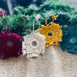 May include: Four handmade macrame ornaments with fringe, each featuring a circular mirror in the center. The ornaments are in shades of red, white, yellow, and green.