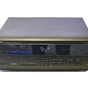 May include: A dark gray Technics SL-MC4 compact disc changer featuring a front-facing digital display showing track information, a numeric keypad, various playback control buttons, and a MASH multi-stage noise shaping logo on the top right corner.