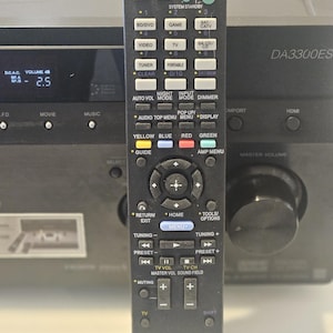 May include: A black remote control with a silver button for the "TV" function. The remote has a variety of buttons, including "Sleep", "Input", "Audio", "Menu", "Tools/Options", "Tuning", "Preset", "TV Vol", "TV Ch", "Master Vol", "Sound Field", "Muting", and "Shift". The remote also has a small screen that displays "DA3300ES".