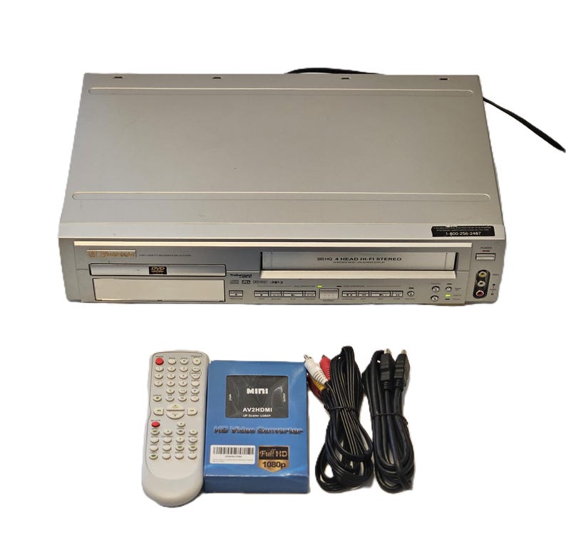May include: Silver DVD/VCR combo player with a remote control, a blue AV2HDMI converter box, and various cables. The player has a DVD tray and a VCR slot. The remote is white with many buttons. The converter box is labeled "MINI AV2HDMI".