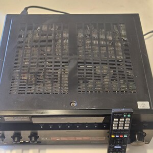 May include: Black Sony receiver with a remote control. The receiver has a dark gray face with knobs and buttons. The top of the receiver has a vented design. The remote control is black with multiple buttons.