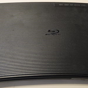 May include: A black Samsung Blu-ray Disc player with a remote control. The player has a sleek, modern design and features a silver logo on the front.