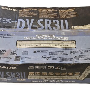 May include: A Sharp DV-SR3U DVD recorder and player box. The box is primarily black and light blue with white text. The box has the words "DVD Recorder" in English, French, and Spanish. The box also has the words "DVD-RW/R Recording & Playback".