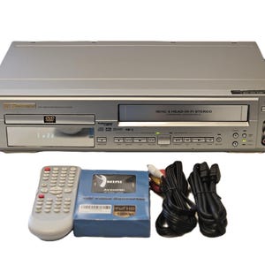 May include: Silver DVD/VCR combo player with a remote, a blue AV/HDMI video converter, and black cables. The player has a DVD tray and a VHS tape slot. The remote is white with many buttons. The converter is in a blue box.