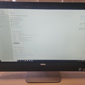 May include: A Dell computer monitor with a black bezel and a silver stand. The screen displays a Windows About page with information about the device specifications and Windows version.