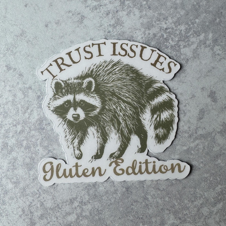 May include: A sticker featuring a detailed illustration of a raccoon in shades of gray and brown. The text "TRUST ISSUES" arches above the raccoon, and "Gluten Edition" is below. The sticker has a white border.