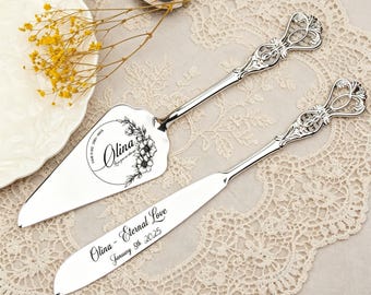 May include: A silver cake server and knife set with ornate handles. The server features the name "Olina" and floral details. The knife is engraved with "Olina - Eternal Love January 5th 2025". The set rests on a lace tablecloth.