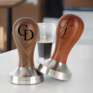 May include: Two wooden coffee tampers with stainless steel bases. One tamper is engraved with the initials "GD" and the other is engraved with the name "Nathaniel".