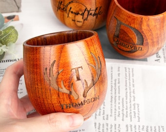 Puede incluir: Tres copas de vino de madera sin pie con un acabado de vetas de madera natural. Una copa presenta el nombre "Donovan", otra "The Found Table", y la tercera tiene una "T" con "Thompson" y cornamentas grabadas.