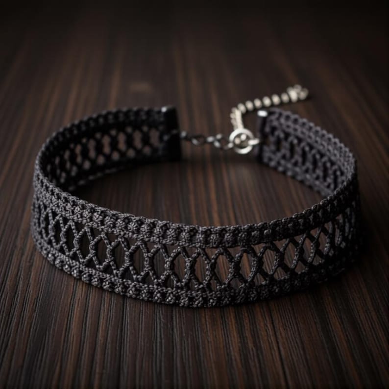 May include: A black choker necklace with an openwork design. The necklace is made of a woven material and features a delicate pattern. The choker has a silver-colored clasp and chain for adjustable sizing. The background is a dark wood surface.