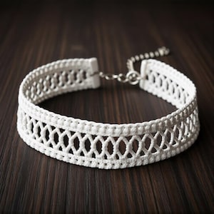 May include: A white crochet choker necklace with a delicate openwork design. The necklace features a repeating diamond pattern and a silver-colored chain clasp. The choker is displayed on a dark wood surface.