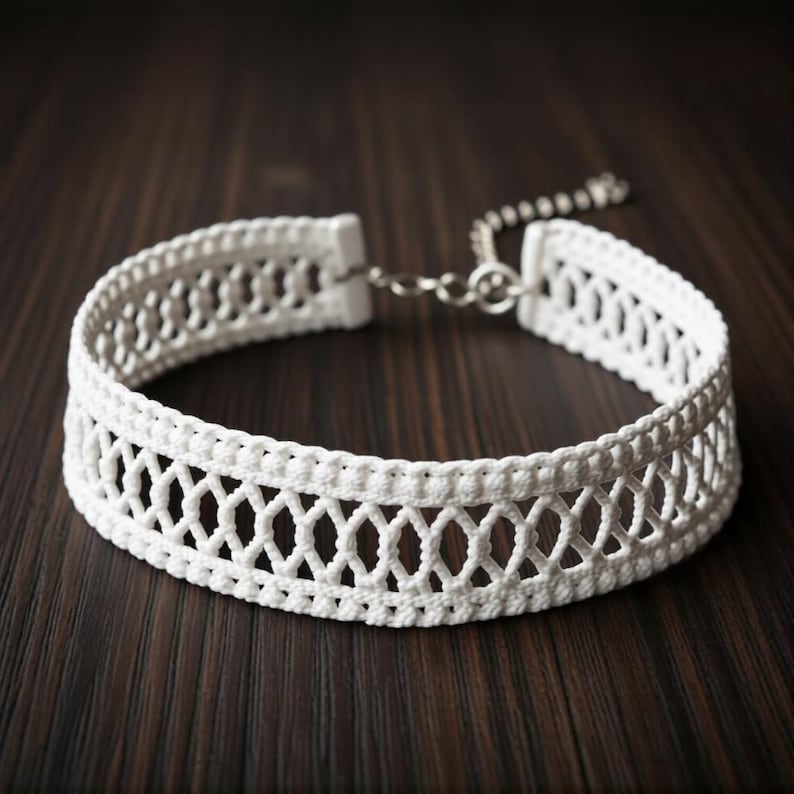 May include: A white crochet choker necklace with a delicate openwork design. The necklace features a repeating diamond pattern and a silver-colored chain clasp. The choker is displayed on a dark wood surface.