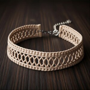 May include: A beige crochet choker necklace with an openwork design. The necklace features a delicate pattern of interconnected diamond shapes. The choker has a chain and clasp closure. The necklace is displayed on a dark brown wooden surface.