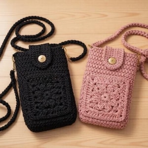 May include: Two crochet phone crossbody bags. One is black, the other is pink. Both have a flap with a wooden button closure and a front pocket with a floral design. The bags have a long, thick strap.