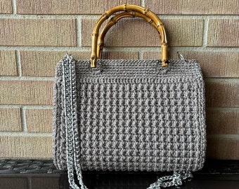May include: A gray crocheted handbag with a bamboo handle and a silver chain strap.