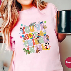 May include: Pink t-shirt with a colorful graphic of Disney characters and the text "You've Gotta Friend in Me."