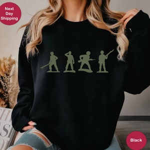 Puede incluir: Sudadera negra con un gr&aacute;fico de cinco soldados de juguete verdes en fila.