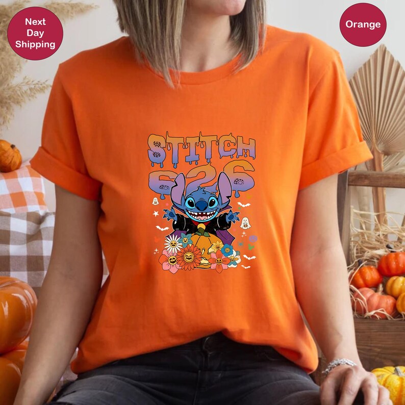 May include: Orange t-shirt with a blue Stitch character dressed as a vampire with the text "Stitch 226" above him. The character is surrounded by Halloween themed imagery like bats, pumpkins, and flowers.