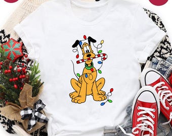 May include: White t-shirt featuring a cartoon Pluto character with a candy cane in its mouth, wrapped in Christmas lights. The shirt has a crew neck and short sleeves. The words "Next Day Shipping" and "White" are in the image.