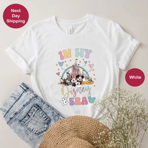 May include: White t-shirt with a graphic of Mickey Mouse and friends in front of Cinderella's Castle. The text "In My Disney Era" is printed on the shirt.