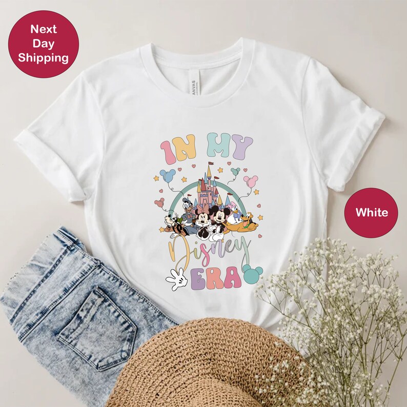May include: White t-shirt with a graphic of Mickey Mouse and friends in front of Cinderella's Castle. The text "In My Disney Era" is printed on the shirt.