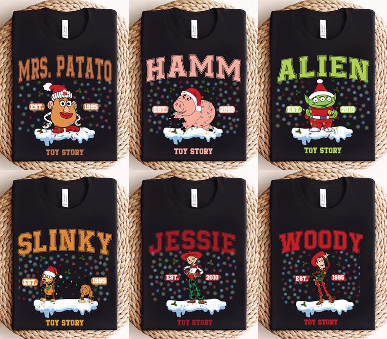 May include: Six black t-shirts with different Toy Story characters printed on them. Each shirt has a festive Christmas theme with a snowy background and colorful lights. The characters include Mrs. Potato Head, Hamm, Alien, Slinky Dog, Jessie, and Woody.