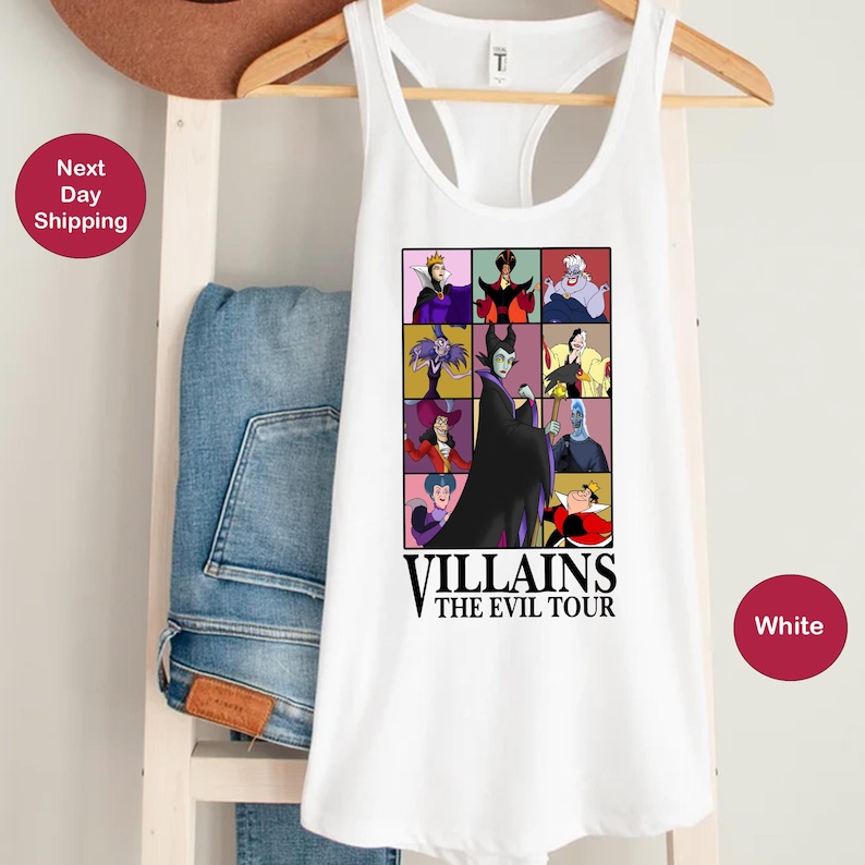 Op de afbeelding: Witte tanktop met een kleurrijke afbeelding van verschillende tekenfilm-schurken. De afbeelding bevat de tekst "Villains The Evil Tour". De tanktop hangt aan een houten kleerhanger.