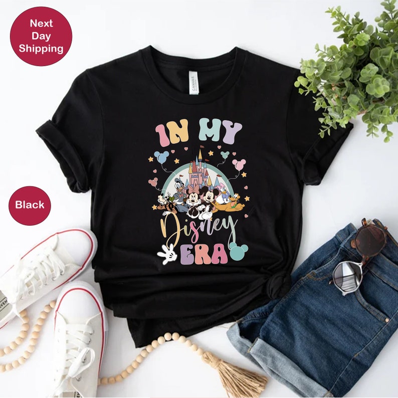 May include: Black t-shirt with a graphic of Mickey Mouse and friends in front of Cinderella's Castle. The text "In My Disney Era" is printed in rainbow colors.