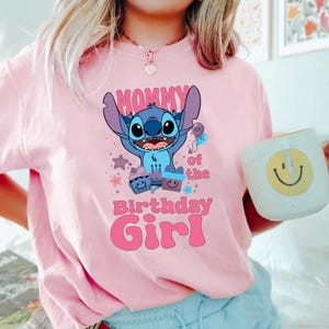 K&ouml;nnte beinhalten: Rosafarbenes T-Shirt mit einer blauen Stitch-Figur aus Lilo & Stitch. Das Shirt tr&auml;gt den Schriftzug "Mommy of the Birthday Girl" in rosa Buchstaben.