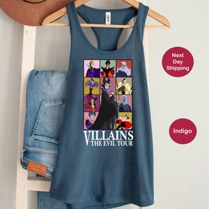 Op de afbeelding: Een blauwe tanktop met een raster van tekenfilm-schurken. De afbeelding bevat personages als Maleficent en de boze koningin, met de tekst "VILLAINS THE EVIL TOUR" onder de afbeeldingen. De tanktop hangt aan een houten hanger.