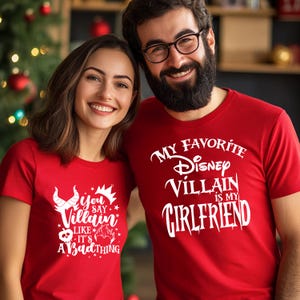 Puede incluir: Una pareja lleva camisetas rojas con un estampado gr&aacute;fico blanco. La camiseta de la mujer dice "You say Villain like it's a bad thing" con una corona y cuernos. La camiseta del hombre dice "My Favorite Disney Villain is my Girlfriend".
