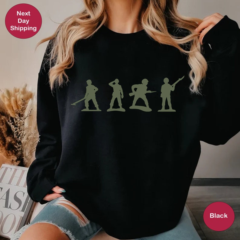 Puede incluir: Sudadera negra con un gr&aacute;fico de cinco soldados de juguete verdes en fila.