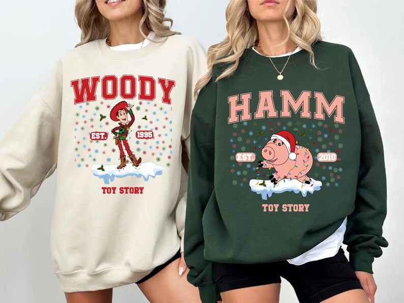 May include: Two cream and green Christmas themed sweatshirts with Toy Story characters. The cream sweatshirt features Woody with the text "WOODY EST. 1995 TOY STORY". The green sweatshirt features Hamm with the text "HAMM EST. 2010 TOY STORY".