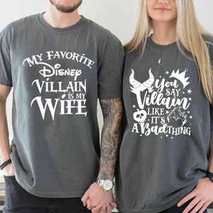 May include: Two gray t-shirts with white text. The first shirt says "My Favorite Disney Villain is My Wife". The second shirt says "You Say Villain Like It's A Bad Thing".