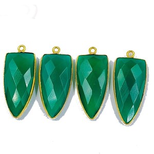 May include: Four green gemstone pendants with gold-toned settings. Each pendant is shaped like a teardrop with a faceted surface.