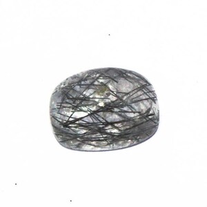 May include: A clear quartz cabochon with black rutile inclusions. The stone is faceted and has a smooth, polished surface.
