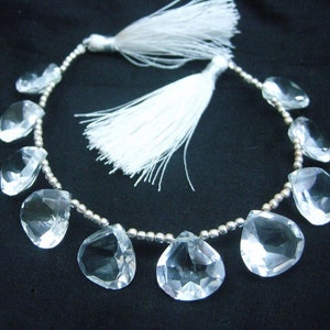 Peut inclure: Un collier de perles de quartz clair facettées en forme de larme. Les perles sont enfilées sur une chaîne argentée avec de petites perles argentées entre chaque pierre précieuse. Le collier est doté de deux glands blancs attachés à la chaîne.