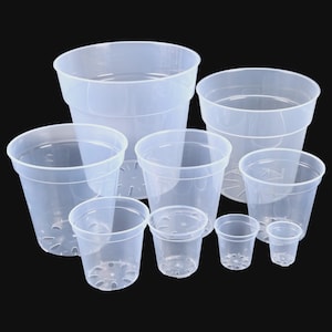 Può includere: Una collezione di vasi per piante in plastica trasparente di varie dimensioni. I vasi sono cilindrici con una parte superiore leggermente svasata e fori di drenaggio sul fondo. Sfondo nero.